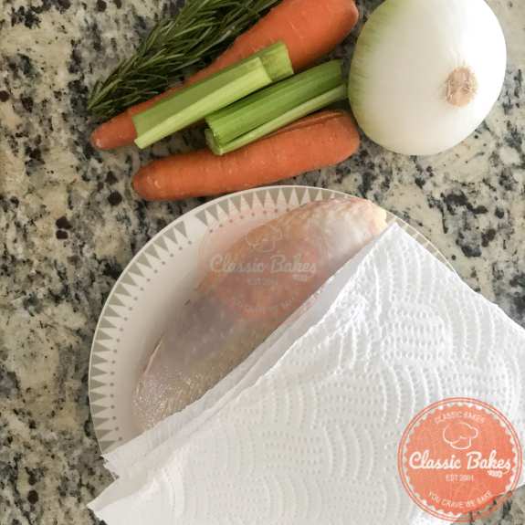 Overview of raw turkey breast on a plate being patted dry with a paper towel 