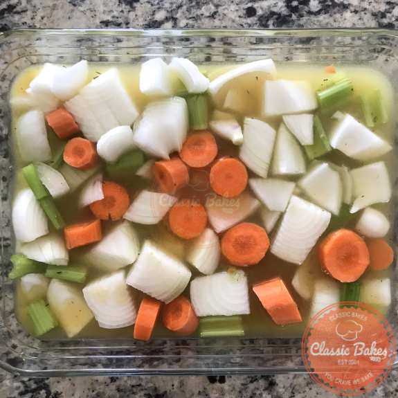 A roasting pan filled with vegetables and chicken stock 
