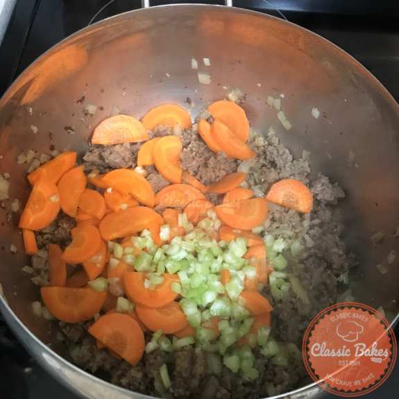 Carrots and celery being added to a pot of soup 