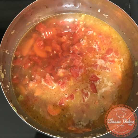 Diced tomatoes and chicken broth being added to a pot of soup