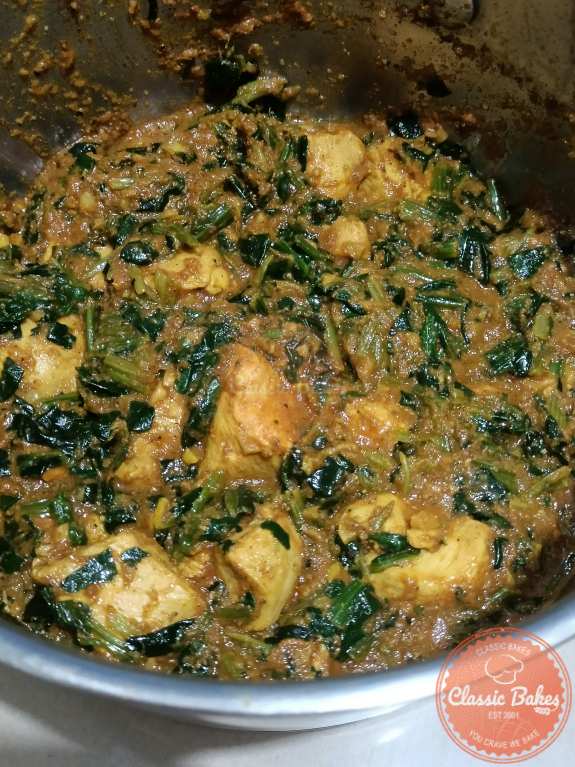 Spinach added into the chicken saag mixture in a pot