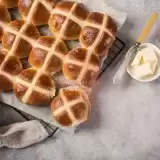 Side shot of a tray of Hot Cross Buns with butter on side