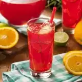 Front shot of Caribbean Fruit Punch in a glass cup on top of cloth with sliced fruits on the side