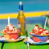 Front shot of Conch Salad in small bowls with drinks on the background