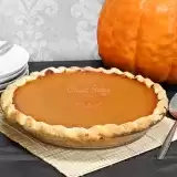 Front shot of Vegan Pumpkin Pie with pumpkin on the back and serving plates and spoon