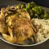 Front shot of Air Fryer Cornish Hen in a plate with rice and brussels sprouts on the side