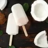 Arial of two coconut popsicles with fresh coconut on a tabletop 