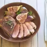 Overview of sliced duck breast with figs in a bowl with a fork and knife on the side 